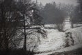 Snowy landscape village rand and fields covered with a thin layer of snow next to a path, stream and trees wintry mood