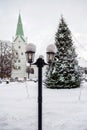 Snowy lantern with decorated Christmas tree and church in blurred background, shallow DOF