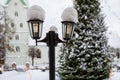 Snowy lantern with decorated Christmas tree and church in blurred background, shallow DOF