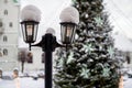 Snowy lantern with decorated Christmas tree and church in blurred background, shallow DOF