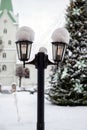 Snowy lantern with decorated Christmas tree and church in blurred background, shallow DOF