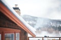 snowy mountain cabin roof with chimney, smoke merging with fog Royalty Free Stock Photo