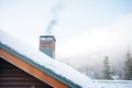 snowy mountain cabin roof with chimney, smoke merging with fog Royalty Free Stock Photo