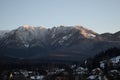 Snowy mountain and houses surrounded by trees under the plain blue sky Royalty Free Stock Photo