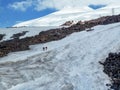 Snowy mountain landscape of Elbrus on a Sunny summer day. The two travelers climb on a snowy road in the mountain