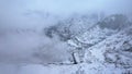 Snowy mountains with coniferous trees in clouds