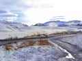 Snowy mountains and ridge  country road with puddle  brown grass in the foreground. Winter landscape Royalty Free Stock Photo