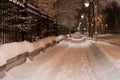 Snowy night pathway in city. Bright light of lanterns. Horizontal view