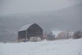 Snowy old black barn in snowstorm with hills