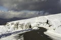 A snowy road curve in the mountains with a cloudy sky - horizontal Royalty Free Stock Photo