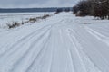 Snowy road in a field leading to pine forest. Winter road to nowhere in sunny day, snow-covered fresh car track. Car