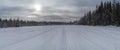 Snowy road through forest with snowmobile tracks in a bright winter day