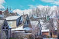 Snowy roofs in upscale neighborhood with spires and chimneys and gables under blue sky