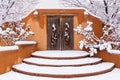 Snowy scene of adobe wall with rustic wood doors and chile ristras Royalty Free Stock Photo