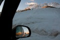 Snowy view from the car window. Sunset in the mountains reflection in rear view mirror. Winter escape