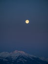 Snowy winter alpine landscape after sunset, pink purple sky with a full moon over a mountain peak