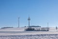 snowy winter landscape with a field, forest, radio tower and wind turbines for power generation Royalty Free Stock Photo