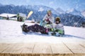 Snowy winter sunshine mountains landscape with family having fun in the snow, wooden board top for products and decorations. Royalty Free Stock Photo