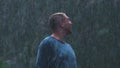 A soaked man looks toward the sky in a cathartic heavy rainstorm.