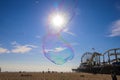 A soap bubble in the sky with people relaxing on the beach and a colorful Ferris wheel and rollercoaster on the pier