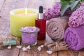 Soap, burning candle, bowl with sea salt, red bottle with aromatic oil, lilac flowers and towels on wooden background Royalty Free Stock Photo