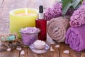 Soap, burning candle, bowls with sea salt, bottle with aromatic oil, lilac flowers and towels on wooden background Royalty Free Stock Photo