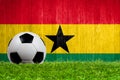 Soccer ball on grass with Ghana flag background