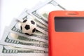 A soccer ball lies on five hundred US dollars next to a mobile phone in a red case. Sports betting concept. Close-up Royalty Free Stock Photo