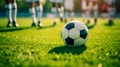 The soccer ball lies on the grass field, in the background out of depth the feet of soccer players, the atmosphere of soccer