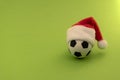 Soccer ball in a red Santa Claus hat. Green background. Copy space. The concept of sports New Year`s gift Royalty Free Stock Photo