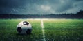 A soccer field with green grass, soccer ball lying on the field, rain coming down