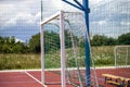 Soccer or football field playground with bright red soft rubber flooring, big gate, empty bench and protective net fence in rural Royalty Free Stock Photo