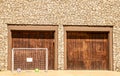 Soccer net and two balls set up in driveway in front of wooden doors of two car garage of rock house