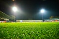 A soccer stadium with a marked green grass pitch with a soccer ball on the center mark at night under illuminated floodlights Royalty Free Stock Photo