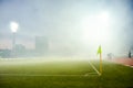 A soccer stadium with a marked green grass pitch with a soccer ball on the center mark at night under illuminated floodlights Royalty Free Stock Photo