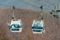 Two gondola cabins of Gorky Gorod cable way ski lift in Sochi full of skiers on bare forest mountain background.