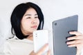 Social Addiction concept with Asian woman holding smart phone and tablet laying down in bed