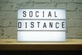 Social Distance word in light box on wooden shelve and white brick wall background