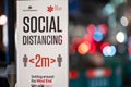 Social Distancing warning sign with out of focus traffic headlights in the background. Shallow depth of field bokeh effect Royalty Free Stock Photo