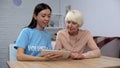 Social worker helping senior lady to cope with tablet, teaching new technologies Royalty Free Stock Photo