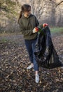 Socially active volunteering - a girl collects garbage against the background of trees and fallen leaves