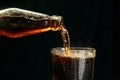 Soda, coke, dark beer pouring from bottle into glass against black background Royalty Free Stock Photo