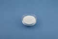 Sodium benzoate, sodium salt of benzoic acid in glass dish on blue background. Food additive E211. White granulated powder,