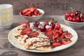 Soft Belgian heart shaped waffles with cherries and strawberries, chocolate topping and powdered sugar on yellow plate. Wooden