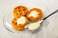 Soft waffles poured condensed milk, spoon in saucer on wooden table Royalty Free Stock Photo