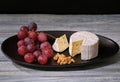 Soft blue cheese, ripe red grapes and walnuts on black dish, aperitif for wine Royalty Free Stock Photo