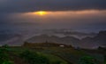 Soft blur of sun rise moment among dark cloud and shine ray light to building and farm with mist cover the mountain Royalty Free Stock Photo