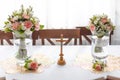 Soft bridal bouquets of fresh flowers in glass vases and church cross on celebratory table in restaurant. Elegant Royalty Free Stock Photo