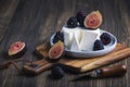 Soft cheese with brambles and fig halfs on a wooden rustic board. Close up dark moody shot, selective focus