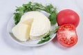 Soft cheese on saucer among the tomatoes, greens on tablecloth Royalty Free Stock Photo